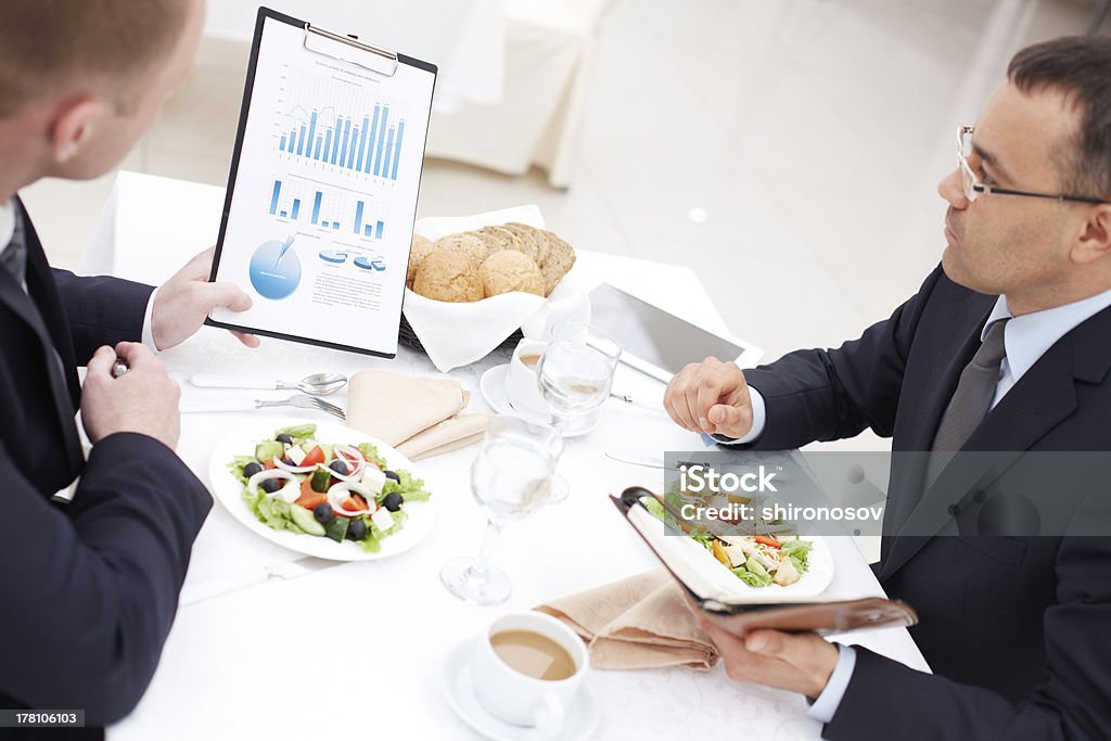 Discussing paper at lunch Confident businessmen discussing paper during business lunch Adult Stock Photo