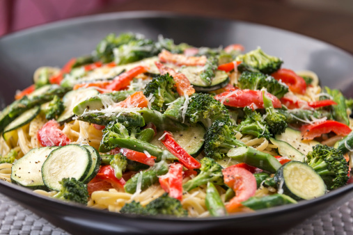 A large pasta bowl is full of delicious Pasta Primavera made with fresh asparagus, broccoli, red bell pepper and zucchini and is served over a bed of linquine.  One image in a series.
