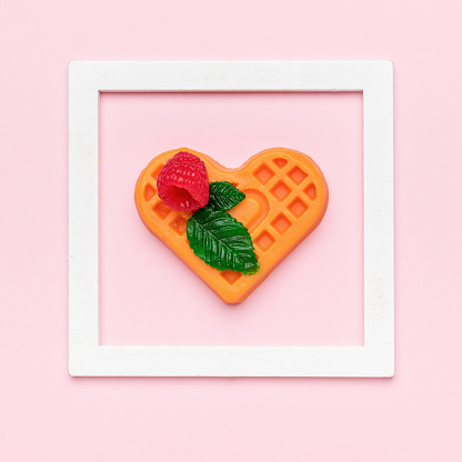 A cookie figurine with a leaf and a berry in a white frame on a pink background. Creative dessert.