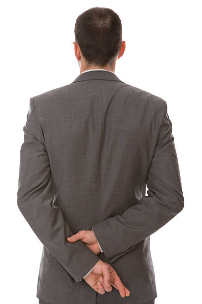 Fingers Crossed A man in a business suit with his fingers crossed behind his back. hands behind back stock pictures, royalty-free photos & images