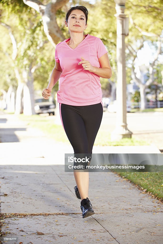 Female Runner Exercising On Suburban Street Female Runner Exercising On Suburban Street Looking Into Distance 30-39 Years Stock Photo