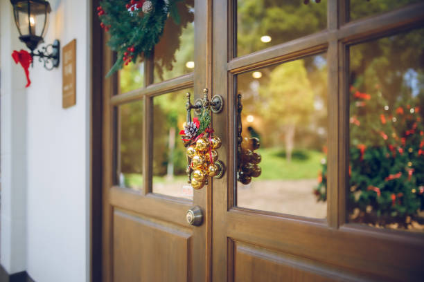 Decorate christmas event on wooden door with small golden bells hanging on the door handle, the background have reflection on the glass of the christmas tree
