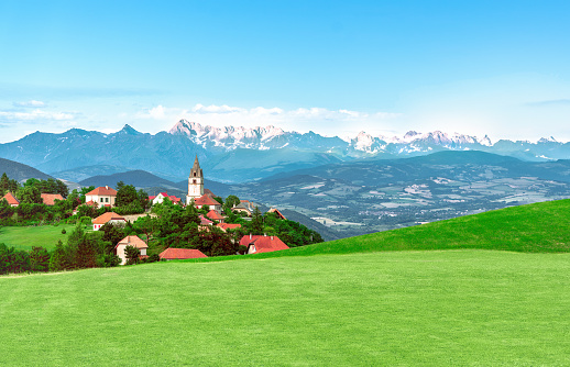 French rural small village in an alpine mountain landscape at green grassy hills and snowy mountains in background - Rural tourism concept.