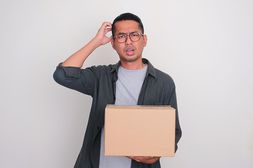 Adult Asian man showing confuse expression while holding a box of package