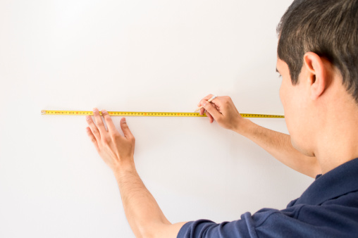 Closeup of people pointing at a measuring tape on the wall and marking with pencil