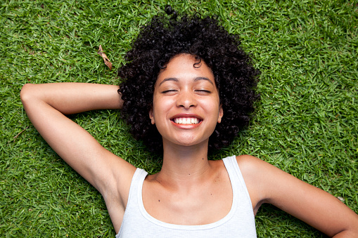 Happy mixed race woman lying down on green grass with hand behind her head.