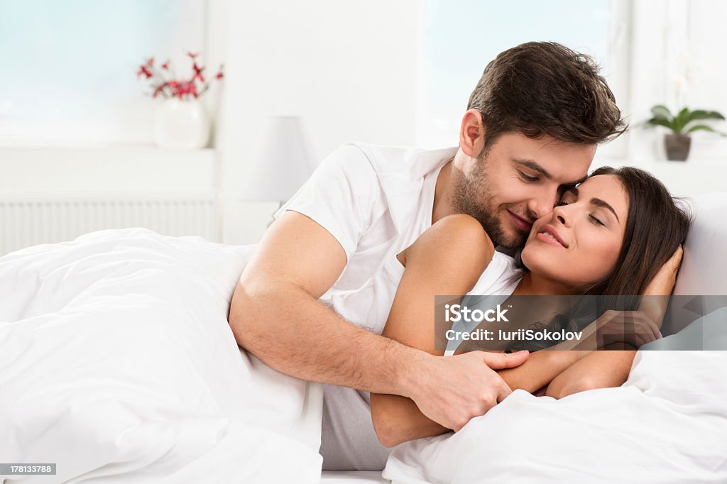 Young adult couple cuddling in their bedroom Young adult heterosexual couple lying on bed in bedroom Adult Stock Photo