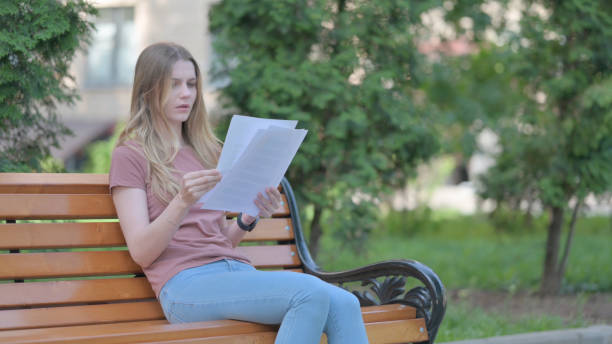 istock Young Woman Feeling Upset while Reading Contract while Sitting Outdoor on a Bench 1781355693