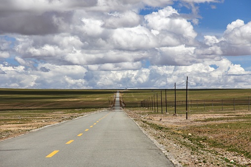 An asphalt road winds through a sun-soaked prairie on a cloudy day
