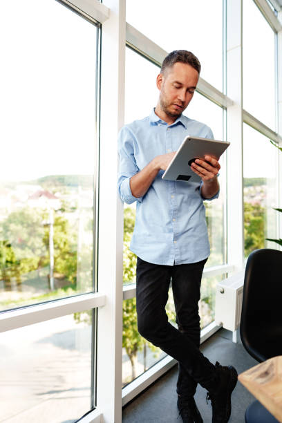 istock Modern businessman using digital tablet while standing near window in his office 1781366746