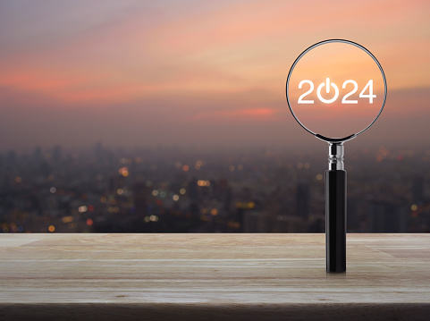 2024 start up flat icon with magnifying glass on wooden table over blur of cityscape on warm light sundown, Business happy new year 2024 cover concept