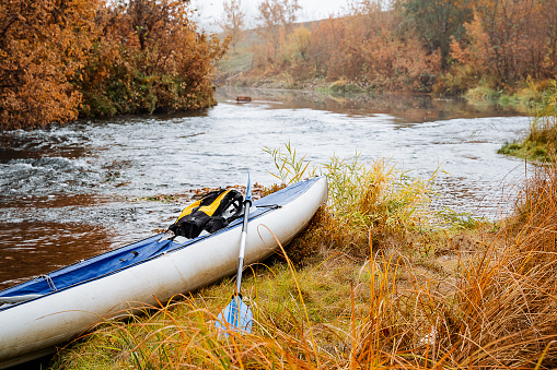 Tourist kayak blue for rafting on mountain rivers stands on the river bank. A yellow backpack lies in the boat. The concept of rafting on taiga rivers. Autumn expedition. High quality photo