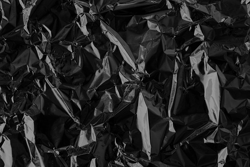 Shiny black foil texture background, pattern of wrapping paper with crumpled and wavy.