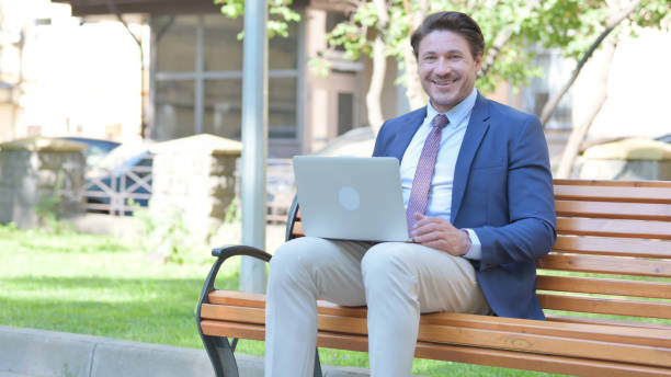 istock Middle Aged Businessman Smiling at Camera while Working on Laptop Outdoor 1781386607