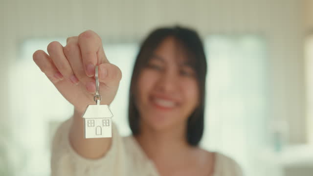 Closeup of young Asian woman smiling looking at camera show new house keychain in living room. Lifestyle spend time in house.