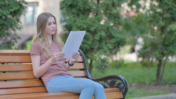 istock Young Woman Reading Documents while Sitting Outdoor on a Bench 1781405501