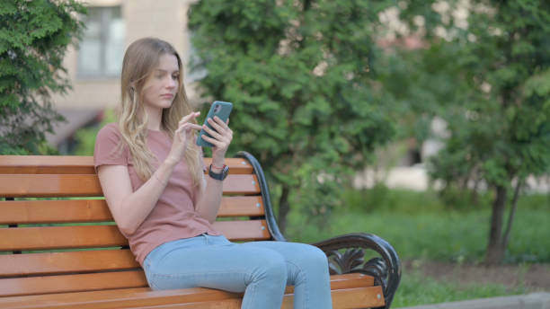 istock Young Woman using Smartphone while Sitting Outdoor on a Bench 1781416702