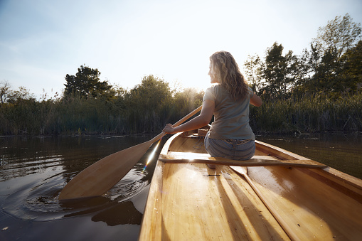 Rear view of happy woman enjoying while paddling a boat during springtime on a river. Copy space.