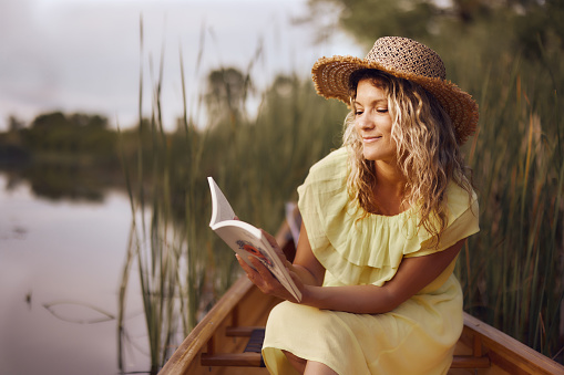 Young smiling woman enjoying in book during spring day in a canoe. Copy space.
