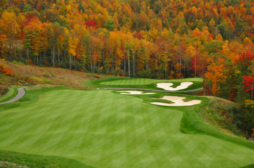 A beautiful golf course in fall. Location is Nova Scotia, Canada. A blazing red maple tree and exceptional turf conditions highlight the scene. Golf in Nova Scotia is very important industry as a number of prominent new courses have been built in the past decade. Courses are rolling and well treed and make for a relaxing and enjoyable golf experience through nature. Nobody is in this image. 