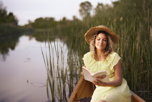 Smiling woman enjoying while reading a book in boat at river. Copy space.