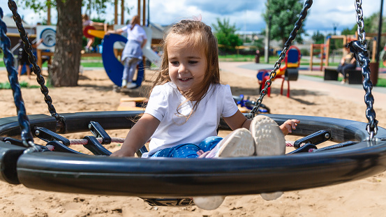 Little girl having fun on a swing on the playground in public park on autumn day. Happy child enjoy swinging. Active outdoors leisure for child.