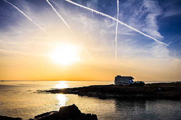 Camper van (RV) at sunset on the beach in Apulia, Italy. Beautiful sky with vapor trails.