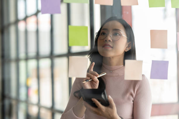 istock Businesswoman using calculator and post-it note on glass wall to calculate and write strategic business plan to develop success. 1781433885