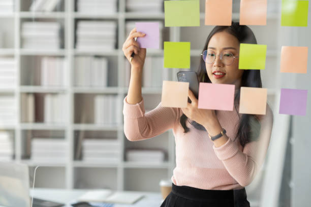 istock Asian businesswoman using mobile phone with pen to write on notepad business plan idea and find flaws to prevent mistakes in work. 1781434394