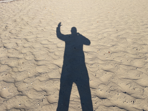 Silhouette of a man standing on the sand with his hands up.
