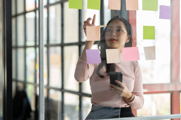 istock Asian businesswoman using mobile phone with pen to write on notepad business plan idea and find flaws to prevent mistakes in work. 1781450062