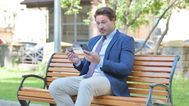 istock Middle Aged Businessman Doing Online Shopping on phone while Sitting Outdoor 1781453349