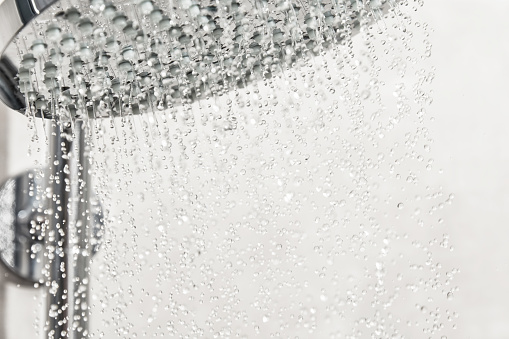 Macro view water drops pours from the metallic shower head. Detailed bathroom equipment