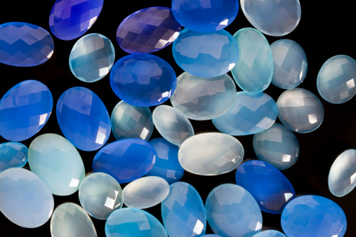 Closeup background picture of faceted natural blue chalcedony and dyed dark aqua chalcedony gemstones on the black background.