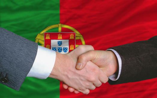 two businessmen shaking hands after good business investment  agreement in portugal, in front of flag