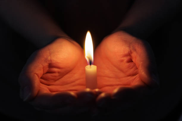 istock Two hands holding a burning candle in dark background 1781482323