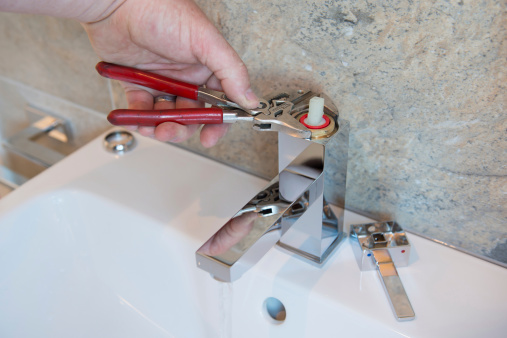 A plumber uses adjustable grips to carry out a repair on a faucet/tap for his client.