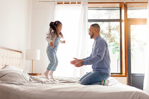 little asian girl jumping on bed at home with dad, korean man playing with daughter, young happy family, dad love concept