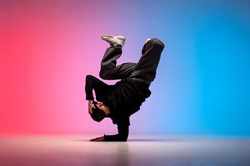young guy hiphop performer break dance in neon club lighting and doing acrobatic trick, male dancer stands in acrobatic pose