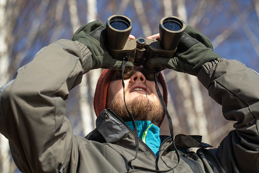 Young man looking through binocular on white background