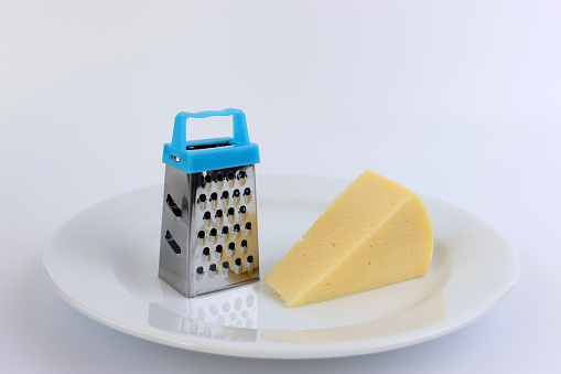 A miniature grater and a piece of cheese on a white plate.