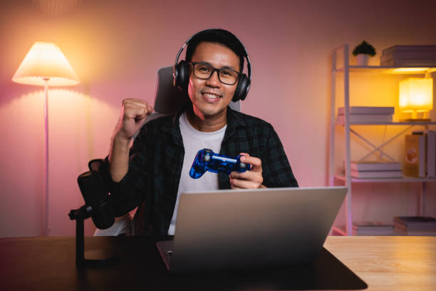 istock Asian influencer man wearing glasses smile cheerful youtuber using joystick playing game live streaming greeting video conference with laptop and wearing headphone. Asian man teaching online concept. 1781518932
