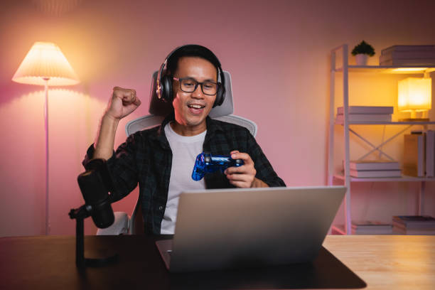 istock Asian influencer man wearing glasses smile cheerful youtuber using joystick playing game live streaming greeting video conference with laptop and wearing headphone. Asian man teaching online concept. 1781518933