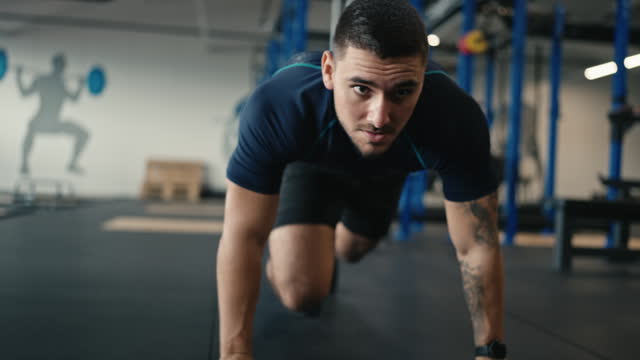Determined Muscular Male Athlete in Sportswear Doing Workout With Legs on Floor and Using Smartwatch at Gym
