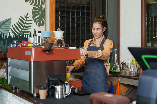 Small business woman Asian woman owns a small cafe and is a family business with an Asian pensioner mother. Making coffee orders for customers at the coffee machine who come to use the cafe service