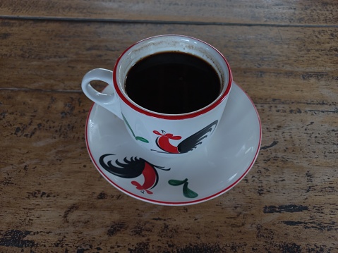 a glass of black coffee with a rooster motif