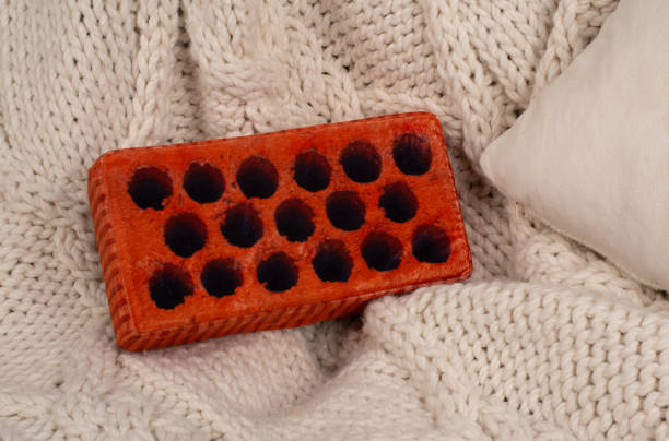 un giocattolo a forma di mattone marrone giace su una coperta sul letto. peluche insoliti - mattoncino - brick red wool heat foto e immagini stock