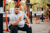 a fat man eats a burger on the playground in the park