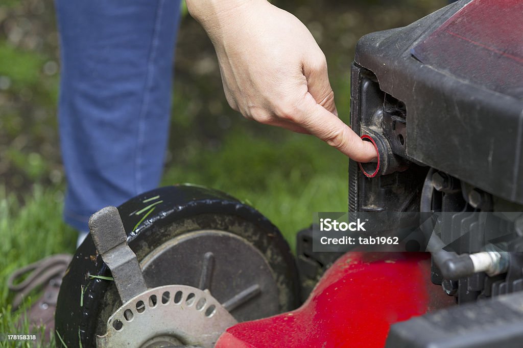 Preparing to start gas lawnmower Horizontal photo of a female hand preparing to start an old gas lawnmower on grass yard with partial blue jeans, shoe and green grass in background Lawn Mower Stock Photo