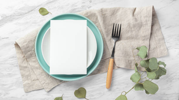 istock Wedding menu card on plate with fork on linen napkin on marble table with green leaves 1781591776